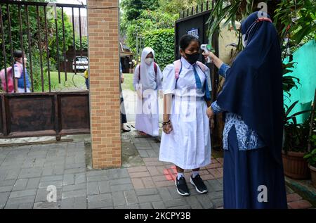 Un insegnante controlla la temperatura corporea di uno studente mentre altri si trovano in coda al loro arrivo in una scuola elementare a Bogor, Giava occidentale, Indonesia, il 18 ottobre 2021, mentre il governo riapre le scuole in mezzo alla pandemia del covid-19. (Foto di Adriana Adie/NurPhoto) Foto Stock