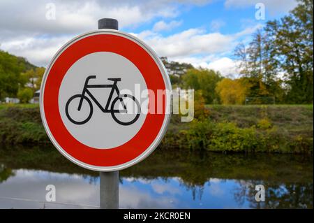 Biciclette vietate o nessun cartello di bicicletta di fronte ad un piccolo fiume e alberi di colore caduta con cielo blu e nuvole bianche puffy che si riflettono nell'acqua Foto Stock