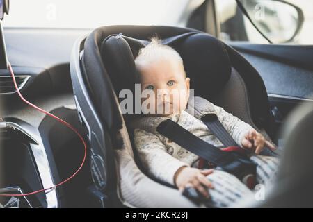 Il bambino piccolo cute ha legato nel sedile dell'automobile del bambino nell'abitacolo durante la guida dell'automobile Foto Stock