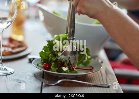 Non è più fresco di questo: Un giovane non identificabile che serve insalata a una cena con gli amici. Foto Stock