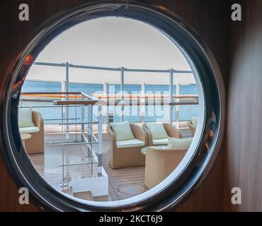 Vista di una lounge all'aperto sul ponte sul lungomare di una nave da crociera attraverso un oblò. Foto Stock