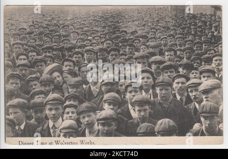 Cena al Wolverton Works, c.1909. Fotografia di un'enorme folla di lavoratori impiegati presso i lavori ferroviari di Wolverton, Buckinghamshire, durante la pausa pranzo. Quasi tutti gli impiegati nella foto sono giovani uomini che indossano i cappellini piatti. Questa cartolina è stata prodotta come parte della serie W.J. Hutchinson, Wolverton, ed è stata pubblicata nel 1909 Foto Stock