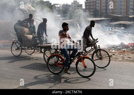 La gente si muove mentre il fuoco di immondizia genera il fumo tossico accanto ad una strada vicino al vecchio canale del fiume Buriganga alla zona di Keraniganj a Dhaka, Bangladesh il 11 novembre 2021. (Foto di Syed Mahamudur Rahman/NurPhoto) Foto Stock