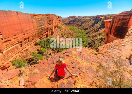 Donna ai margini del Kings Canyon nel Parco Nazionale di Watarrka, il Red Center dell'Australia. Riposa dopo il trekking sul Rim Walk lungo il bordo del canyon nel nord Foto Stock