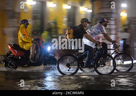 Un motociclista e due ciclisti attraversano la strada principale allagata di Valladolid. Forti piogge nella penisola di Yucatán hanno rallentato il traffico e inondato le strade del centro di Valladolid. Venerdì 19 novembre 2021 a Valladolid, Yucatan, Messico. (Foto di Artur Widak/NurPhoto) Foto Stock