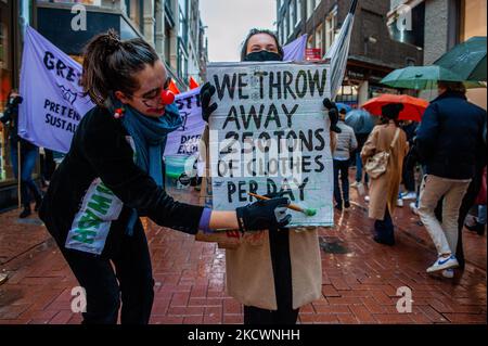 Un clown che rappresenta le pratiche di lavaggio del verde condotte dai marchi della moda, finge di dipingere con vernice verde, durante una sfilata di moda beffa Fast organizzata da XR, contro il Black Friday ad Amsterdam, il 27th novembre 2021. (Foto di Romy Arroyo Fernandez/NurPhoto) Foto Stock