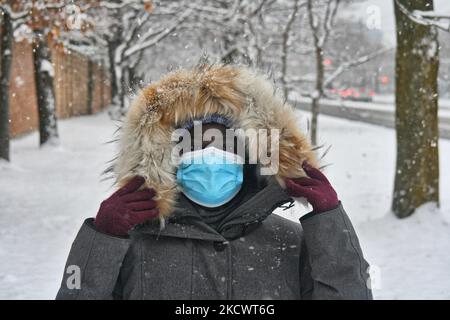 Donna che indossa una maschera facciale mentre cammina in una tempesta di neve durante la pandemia del nuovo coronavirus (COVID-19) a Toronto, Ontario, Canada il 28 novembre 2021. L'Ontario ha riferito il suo più alto numero di casi giornalieri COVID-19 in quasi sei mesi con 964 nuovi casi e un ulteriore decesso. Il Ministero della Salute dice che 498 dei casi di domenica sono tra le persone non vaccinate, 21 sono persone con una dose di vaccino COVID-19, 396 sono completamente vaccinate e 49 sono in persone con stato di vaccinazione sconosciuto. Ciò avviene in un momento in cui i paesi di tutto il mondo sono in forte allerta a causa dell'emergere del nuovo Omicron COVI, più contagioso Foto Stock