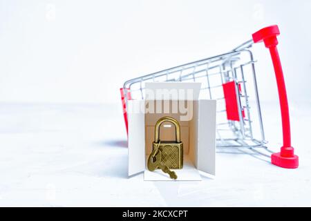 Carrello per la spesa in miniatura rovesciato con scatola di consegna e lucchetto con chiave. Foto Stock