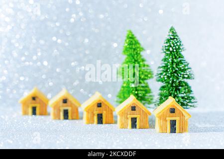 Gruppo di cottage simili in legno posto da due alberi di Natale giocattolo su sfondo scintillante. Concetto di tour delle vacanze invernali. Foto Stock