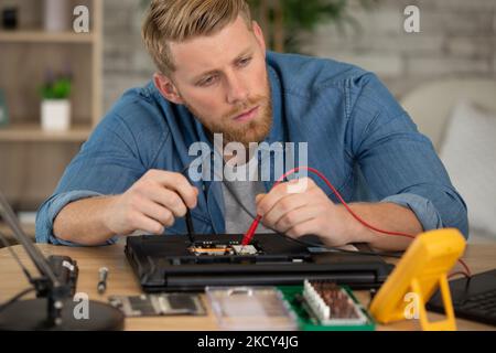 il tecnico ripara il computer portatile utilizzando un multimetro per la misurazione della tensione Foto Stock