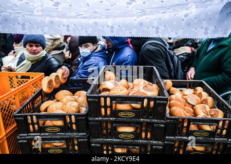 I rotoli sono distribuiti durante la cena della vigilia di Natale per i senzatetto e i poveri durante la pandemia di coronavirus nella piazza principale di Cracovia, in Polonia, il 19 dicembre 2021. La festa di Natale è stata organizzata per la 25tht volta da Jan Kosciuszko, il proprietario del ristorante locale e filantropo. Dalla mattina sono state servite migliaia di porzioni di cibo, con pierogi tradizionali polacchi (gnocchi), carpe fritte, cavolo in umido (bigos) e zuppa di borsch rosso. (Foto di Beata Zawrzel/NurPhoto) Foto Stock