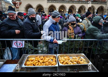 Gli gnocchi tradizionali (pierogi) vengono distribuiti durante la cena della vigilia di Natale per i senzatetto e i poveri durante la pandemia di coronavirus nella piazza principale di Cracovia, in Polonia, il 19 dicembre 2021. La festa di Natale è stata organizzata per la 25tht volta da Jan Kosciuszko, il proprietario del ristorante locale e filantropo. Dalla mattina sono state servite migliaia di porzioni di cibo, con pierogi tradizionali polacchi (gnocchi), carpe fritte, cavolo in umido (bigos) e zuppa di borsch rosso. (Foto di Beata Zawrzel/NurPhoto) Foto Stock