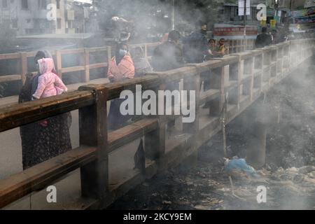 La gente si muove mentre il fuoco di immondizia genera il fumo tossico accanto ad una strada vicino al vecchio canale del fiume Buriganga alla zona di Keraniganj a Dhaka, Bangladesh il 20 dicembre 2021. (Foto di Syed Mahamudur Rahman/NurPhoto) Foto Stock