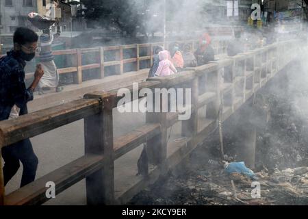 La gente si muove mentre il fuoco di immondizia genera il fumo tossico accanto ad una strada vicino al vecchio canale del fiume Buriganga alla zona di Keraniganj a Dhaka, Bangladesh il 20 dicembre 2021. (Foto di Syed Mahamudur Rahman/NurPhoto) Foto Stock