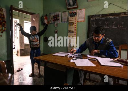 Il capomastro sta facendo un foglio del contrassegno e gli allievi giocano con la corda di salto ed entrano ripetutamente nella stanza dell'ufficio ad una scuola primaria rurale a Nabin Nagar, Bengala occidentale, India il 21/12/2021. (Foto di Soumyabrata Roy/NurPhoto) Foto Stock