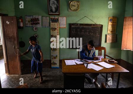 Il capomastro sta facendo un foglio del contrassegno e gli allievi giocano con la corda di salto ed entrano ripetutamente nella stanza dell'ufficio ad una scuola primaria rurale a Nabin Nagar, Bengala occidentale, India il 21/12/2021. (Foto di Soumyabrata Roy/NurPhoto) Foto Stock