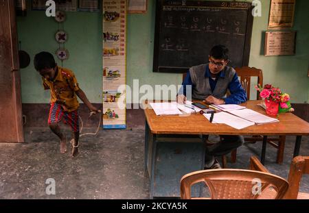 Il capomastro sta facendo un foglio del contrassegno e gli allievi giocano con la corda di salto ed entrano ripetutamente nella stanza dell'ufficio ad una scuola primaria rurale a Nabin Nagar, Bengala occidentale, India il 21/12/2021. (Foto di Soumyabrata Roy/NurPhoto) Foto Stock