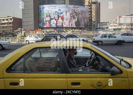 Un conducente di taxi giallo iraniano siede al suo veicolo che è parcheggiato in un angolo di una piazza nel centro di Teheran il 30 dicembre 2021, Come un tabellone gigante con un ritratto simbolico del capo ufficiale militare iraniano generale Qasem Soleimani (C) che è stato ucciso in un attacco di droni nel 2020 a Baghdad, è impiccato su un edificio governativo. Generale Qasem Soleimani . Iran per celebrare il secondo anniversario di morte dell'ex comandante del corpo della Guardia rivoluzionaria Islamica (IRGC) Quds Force, Generale Qasem Soleimani, che ha ucciso in un attacco di droni USA all'aeroporto internazionale di Baghdad in Iraq. (Foto di Mo Foto Stock