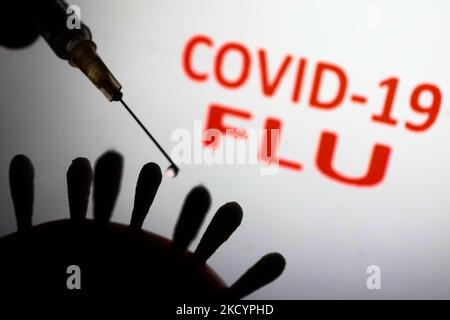 Il modello di coronavirus e la siringa medica sono visti con i segni 'covid-19' e 'flu' visualizzati sullo sfondo in questa foto di illustrazione scattata in Polonia il 4 gennaio 2022. Alcuni paesi hanno riportato casi di pazienti che erano stati infettati sia COVID-19 che influenza. (Foto di Jakub Porzycki/NurPhoto) Foto Stock