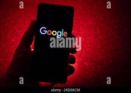 Logo Google su uno smartphone tenuto da una mano con sfondo rosso scuro. Logo Google closeup visualizzato su uno schermo del telefono, smartphone il logo o il motore di ricerca in vari sfondi come la tastiera, la texture illuminata scura o uno schermo del computer, come si vede in questa illustrazione di esposizione multipla, il simbolo dell'azienda è riconosciuto a livello globale. Google, LLC è un colosso tecnologico americano, una multinazionale che si specializza nei servizi e nei prodotti connessi a Internet, che includono le tecnologie di pubblicità online, un motore di ricerca, il cloud computing, il software e l'hardware. È considerato o Foto Stock