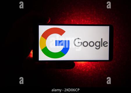 Logo Google su uno smartphone tenuto da una mano con sfondo rosso scuro. Logo Google closeup visualizzato su uno schermo del telefono, smartphone il logo o il motore di ricerca in vari sfondi come la tastiera, la texture illuminata scura o uno schermo del computer, come si vede in questa illustrazione di esposizione multipla, il simbolo dell'azienda è riconosciuto a livello globale. Google, LLC è un colosso tecnologico americano, una multinazionale che si specializza nei servizi e nei prodotti connessi a Internet, che includono le tecnologie di pubblicità online, un motore di ricerca, il cloud computing, il software e l'hardware. È considerato o Foto Stock