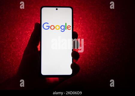 Logo Google su uno smartphone tenuto da una mano con sfondo rosso scuro. Logo Google closeup visualizzato su uno schermo del telefono, smartphone il logo o il motore di ricerca in vari sfondi come la tastiera, la texture illuminata scura o uno schermo del computer, come si vede in questa illustrazione di esposizione multipla, il simbolo dell'azienda è riconosciuto a livello globale. Google, LLC è un colosso tecnologico americano, una multinazionale che si specializza nei servizi e nei prodotti connessi a Internet, che includono le tecnologie di pubblicità online, un motore di ricerca, il cloud computing, il software e l'hardware. È considerato o Foto Stock