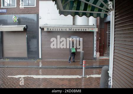 Vita quotidiana ad Amsterdam con persone che passano di fronte a caffè, bar e ristoranti chiusi. Locali e alcuni turisti nelle tranquille strade di Amsterdam durante il blocco nella capitale olandese con negozi e negozi che appaiono con chiuso con la tapparella metallica giù, caffè, bar e ristoranti anche chiusi con tavoli e sedie delle terrazze chiuse. I Paesi Bassi sono stati la prima nazione europea a dichiarare il blocco completo per combattere la nuova variante di Omicron che si surge. Dopo un improvviso ordine governativo prima di Natale, il paese ha chiuso tutti i negozi non essenziali, caffè, ristoranti, ba Foto Stock