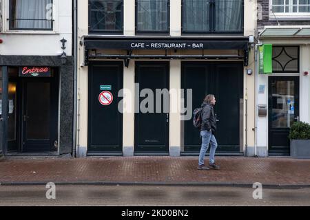 Vita quotidiana ad Amsterdam con persone che passano di fronte a caffè, bar e ristoranti chiusi. Locali e alcuni turisti nelle tranquille strade di Amsterdam durante il blocco nella capitale olandese con negozi e negozi che appaiono con chiuso con la tapparella metallica giù, caffè, bar e ristoranti anche chiusi con tavoli e sedie delle terrazze chiuse. I Paesi Bassi sono stati la prima nazione europea a dichiarare il blocco completo per combattere la nuova variante di Omicron che si surge. Dopo un improvviso ordine governativo prima di Natale, il paese ha chiuso tutti i negozi non essenziali, caffè, ristoranti, ba Foto Stock