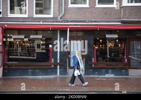 Vita quotidiana ad Amsterdam con persone che passano di fronte a caffè, bar e ristoranti chiusi. Locali e alcuni turisti nelle tranquille strade di Amsterdam durante il blocco nella capitale olandese con negozi e negozi che appaiono con chiuso con la tapparella metallica giù, caffè, bar e ristoranti anche chiusi con tavoli e sedie delle terrazze chiuse. I Paesi Bassi sono stati la prima nazione europea a dichiarare il blocco completo per combattere la nuova variante di Omicron che si surge. Dopo un improvviso ordine governativo prima di Natale, il paese ha chiuso tutti i negozi non essenziali, caffè, ristoranti, ba Foto Stock