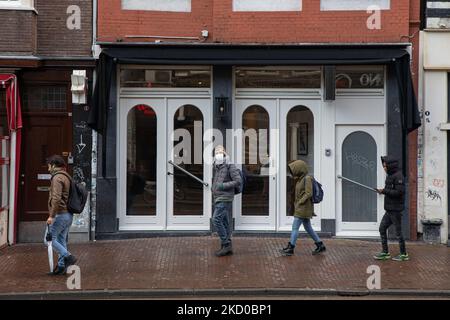 Vita quotidiana ad Amsterdam con persone che passano di fronte a caffè, bar e ristoranti chiusi. Locali e alcuni turisti nelle tranquille strade di Amsterdam durante il blocco nella capitale olandese con negozi e negozi che appaiono con chiuso con la tapparella metallica giù, caffè, bar e ristoranti anche chiusi con tavoli e sedie delle terrazze chiuse. I Paesi Bassi sono stati la prima nazione europea a dichiarare il blocco completo per combattere la nuova variante di Omicron che si surge. Dopo un improvviso ordine governativo prima di Natale, il paese ha chiuso tutti i negozi non essenziali, caffè, ristoranti, ba Foto Stock