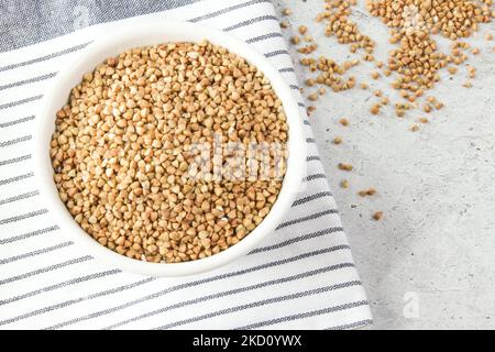 Grano saraceno verde crudo in una ciotola bianca grano saraceno su tovagliolo, fondo di pietra Foto Stock