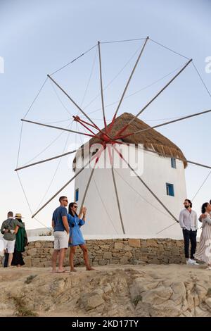 Turisti ai mulini a vento che guardano il tramonto. Gli iconici mulini a vento dell'isola di Mykonos nelle isole Cicladi, Grecia. Mykonos è un'isola della Grecia nel Mar Egeo. Ci sono 16 mulini a vento sull'isola, 5 dei quali sopra Chora, la città principale dell'isola. I mulini a vento sono stati costruiti nel 16th ° secolo dai veneziani, ma le loro costruzioni continuarono fino al 20th ° secolo. Tramonto con la gente ai mulini a vento a Mykonos. I turisti possono ammirare un bellissimo tramonto durante l'ora magica dell'isola di Mykonos in Grecia. L'isola greca di Myconos è una popolare meta turistica mediterranea per i viaggi di h Foto Stock