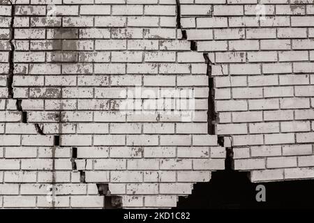 Muro esterno in mattoni con danni estremi crepe che trattengono dalla collisione del veicolo.Seppia foto in bianco e nero astratto foto di sfondo. Foto Stock