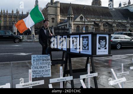 LONDRA, REGNO UNITO - 27 GENNAIO 2022: Un dimostratore tiene una bandiera irlandese accanto a croci simboliche e a una bara con nomi e immagini delle vittime della Bloody Sunday al di fuori delle Case del Parlamento durante una veglia commemorativa del 50th° anniversario della Bloody Sunday e una protesta contro le proposte del governo britannico per l'amnistia per il Le forze statali hanno partecipato il 27 gennaio 2022 a Londra, Inghilterra. Domenica 30 gennaio 1972, i soldati britannici hanno aperto il fuoco su civili disarmati partecipando a una marcia per i diritti civili a Derry uccidendo tredici e ferendo quindici persone, con il giorno del divenire Foto Stock