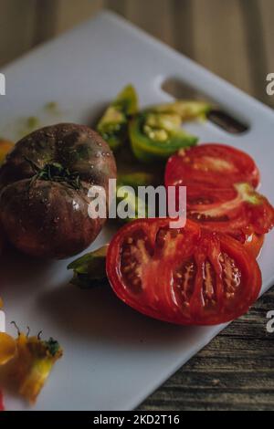affettare i pomodori di cimelio di colore diverso sul tagliere bianco di plastica Foto Stock