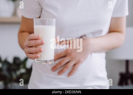 Primo piano di una giovane donna malsana e irriconoscibile che tiene un bicchiere di latte con mal di stomaco a causa dell'intolleranza al lattosio. Problema di salute con dai Foto Stock