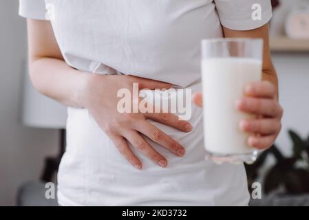 Primo piano di una giovane donna caucasica malsana che tiene un bicchiere di latte con mal di stomaco a causa di intolleranza al lattosio. Problema di salute con latteria f Foto Stock