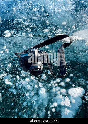 Fotocamera fotografica professionale sul ghiaccio del lago Baikal contro il ghiaccio con sfondo di schiacciamento nella soleggiata giornata invernale. Concetto di viaggio e vacanza Foto Stock