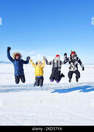 Gruppo di amici turistici felici saltando sullo sfondo di ghiaccio inverno lago Baikal in giornata di sole. Inverno lago Baikal, Russia. Concetto di libertà, viaggiare un Foto Stock