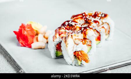 Un primo piano di una serie di deliziosi panini freschi di sushi coperti in salsa su un piatto bianco Foto Stock