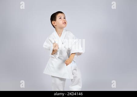 Un ragazzino in kimono pratica il karate su sfondo bianco. Foto Stock