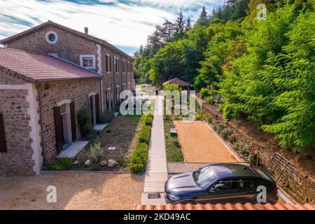 Una bella foto di una grande villa in pietra con un sentiero, giardino privato, auto nera, alberi intorno sulla destra Foto Stock