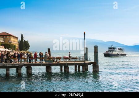 Traghetto sul Lago di Garda, vista in estate delle persone che si trovano sul molo della stazione di Gardone Riviera in attesa dell'arrivo di un traghetto, Lombardia, Italia Foto Stock