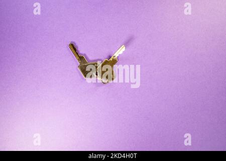 primo piano di un paio di chiavi lucchetti in argento - una piegata di forma isolata su uno sfondo viola Foto Stock