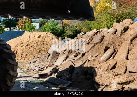 Cantiere con cumulo di vecchie lastre di pietra su sfondo sfocato della benna dell'escavatore Foto Stock