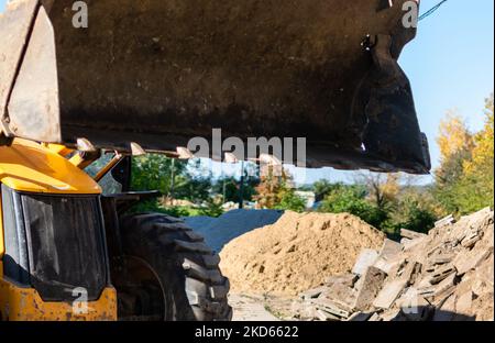 Primo piano della benna dell'escavatore sullo sfondo sfocato del cantiere con un mucchio di sabbia e vecchi blocchi di pietra Foto Stock