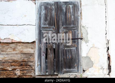 Persiane finestre in legno fatiscenti di vecchia casa abbandonata su pareti bianche Foto Stock