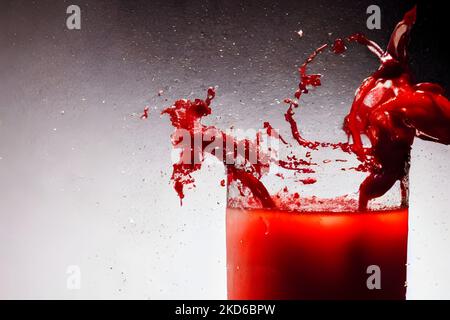 Un primo piano di succo di pomodoro che si spruzzi sul bicchiere su sfondo grigio Foto Stock