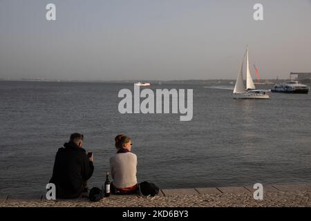La gente assiste al tramonto sulla riva del fiume Tago a Lisbona, in Portogallo, il 29 marzo 2022. (Foto di Manuel Romano/NurPhoto) Foto Stock