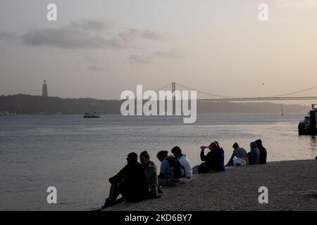 La gente assiste al tramonto sulla riva del fiume Tago a Lisbona, in Portogallo, il 29 marzo 2022. (Foto di Manuel Romano/NurPhoto) Foto Stock